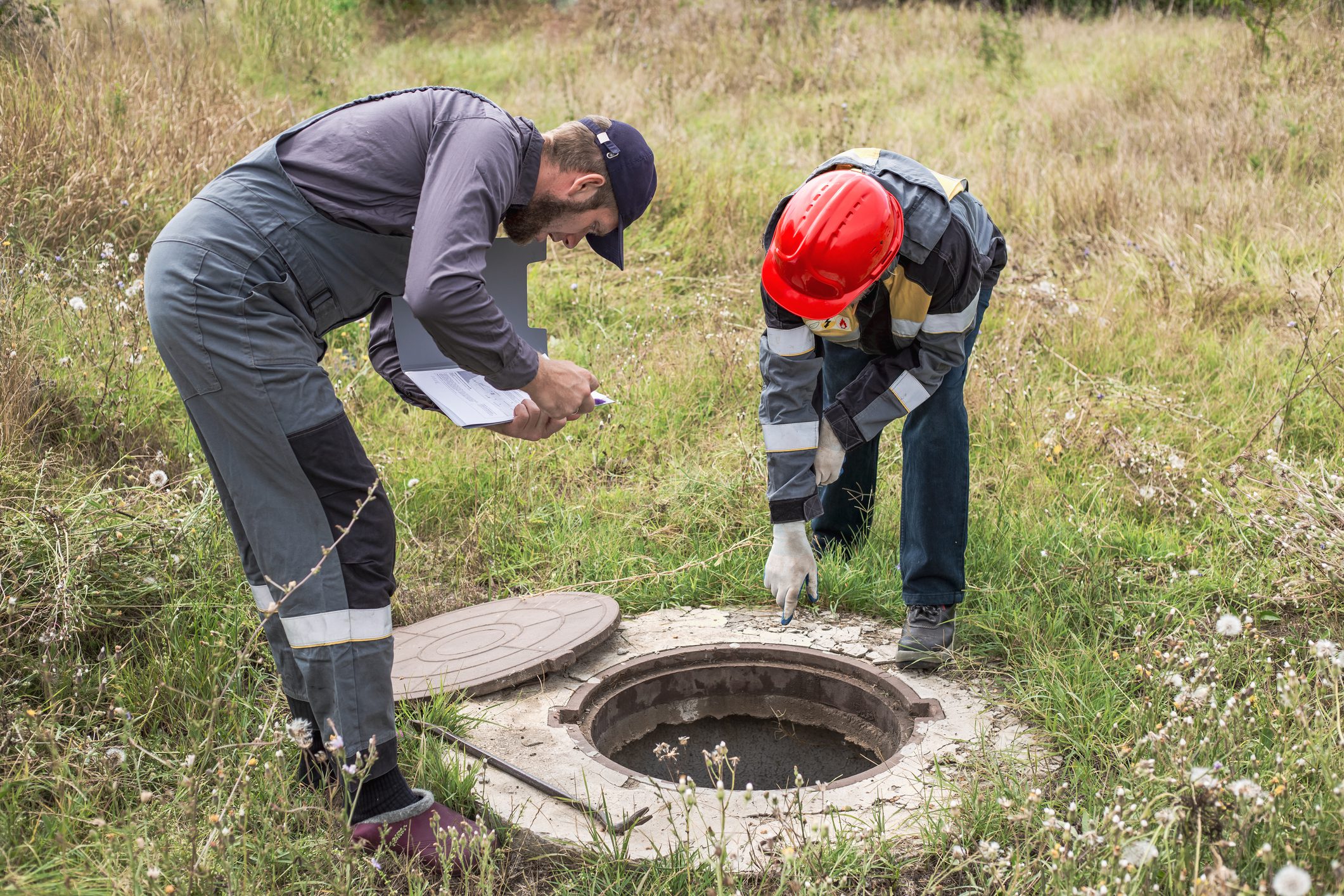 Two workers inspecting open manhole cover.